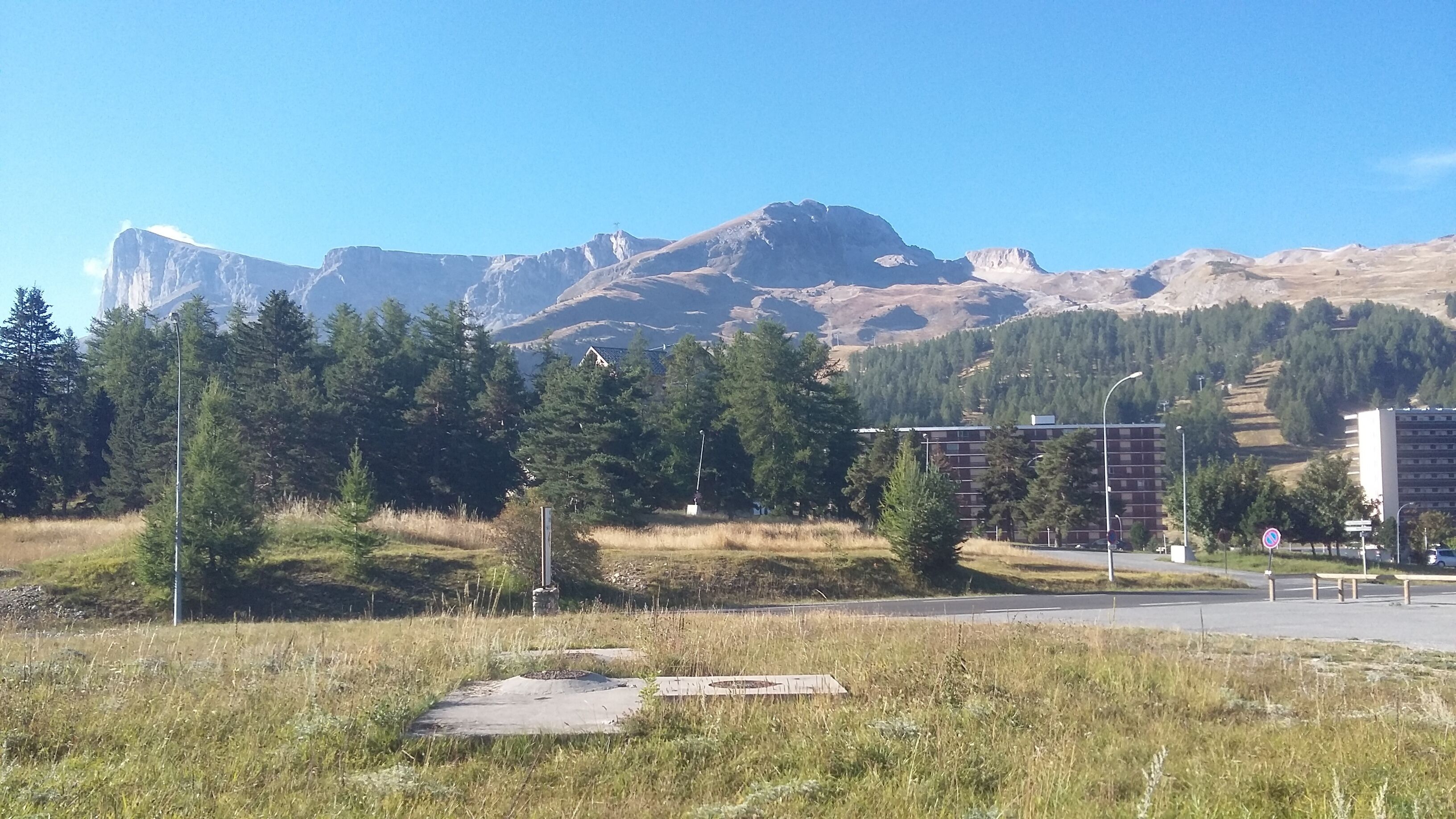 Un paisaje montañoso con una carretera, árboles y un edificio al fondo.