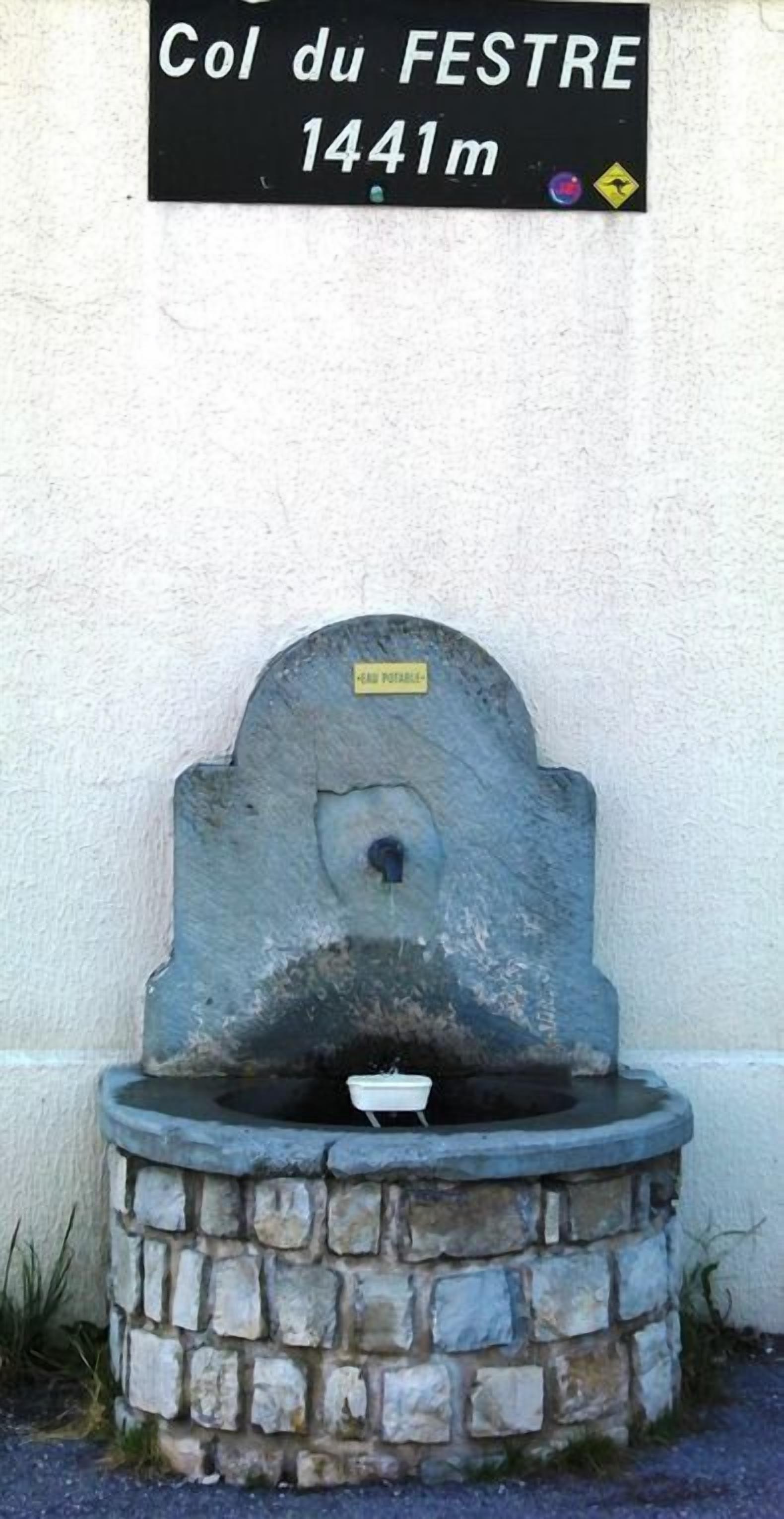 A stone fountain with a sign above it reading "Col du FESTRE 1441m".