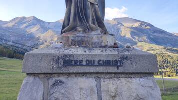 A statue of the Virgin Mary with a child, titled "MERE DU CHRIST," set against a mountainous backdrop.