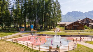 A water park with a circular play area, wooden cabins, and a mountainous backdrop. - Superdevoluy545S (Le Dévoluy)