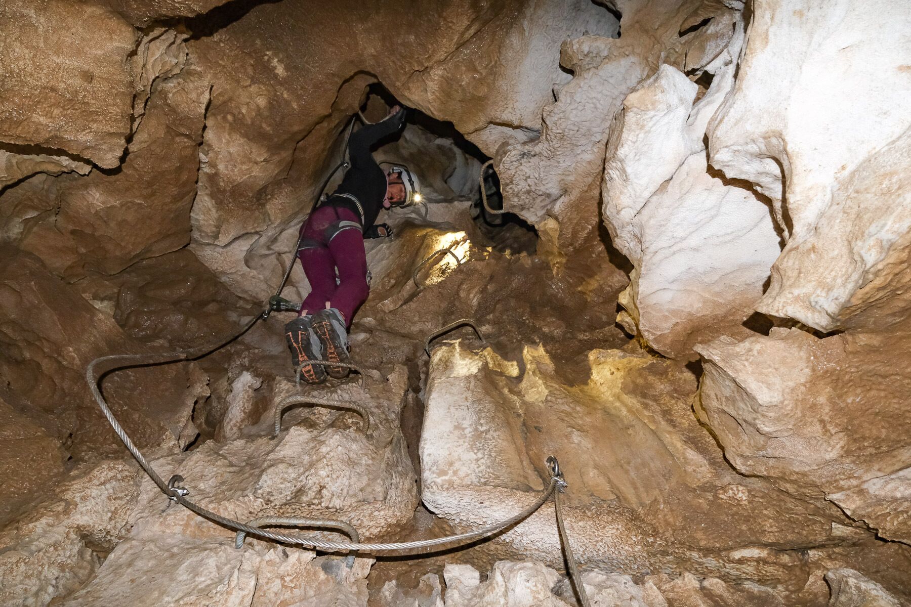 A person climbing a rocky cave wall with safety ropes.