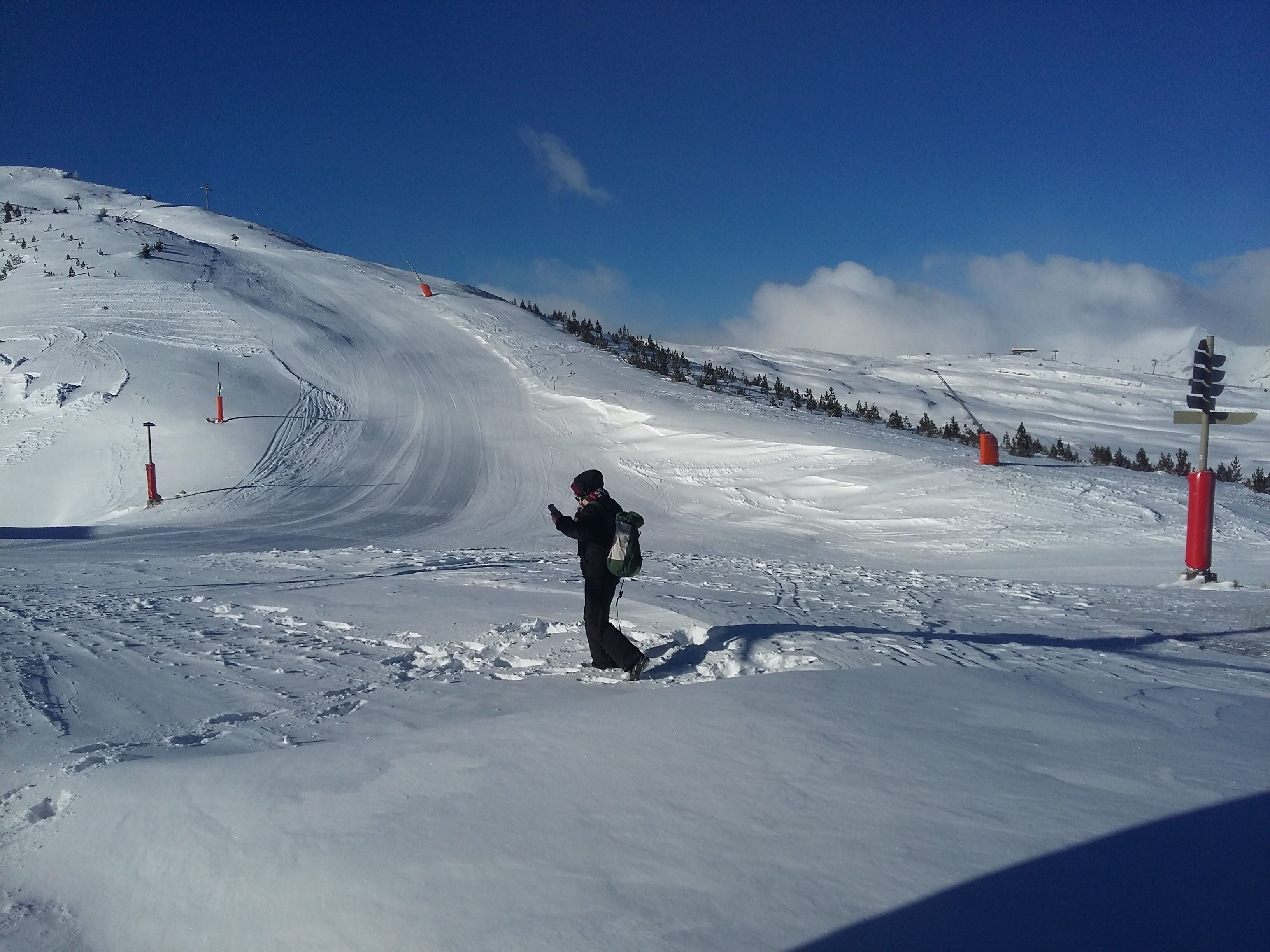 A snowy ski slope with a person standing in the middle, wearing a backpack and a helmet.