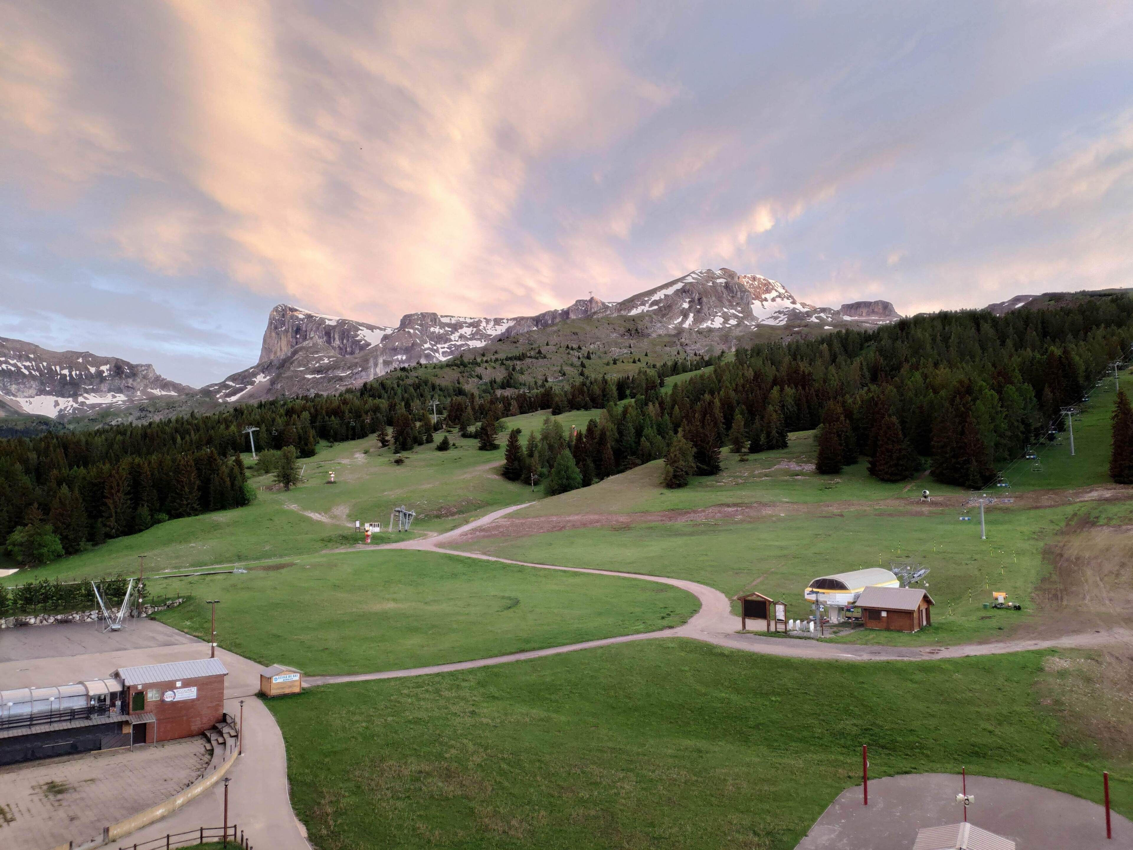 A mountainous landscape with a ski lift, a small building, and a grassy area.