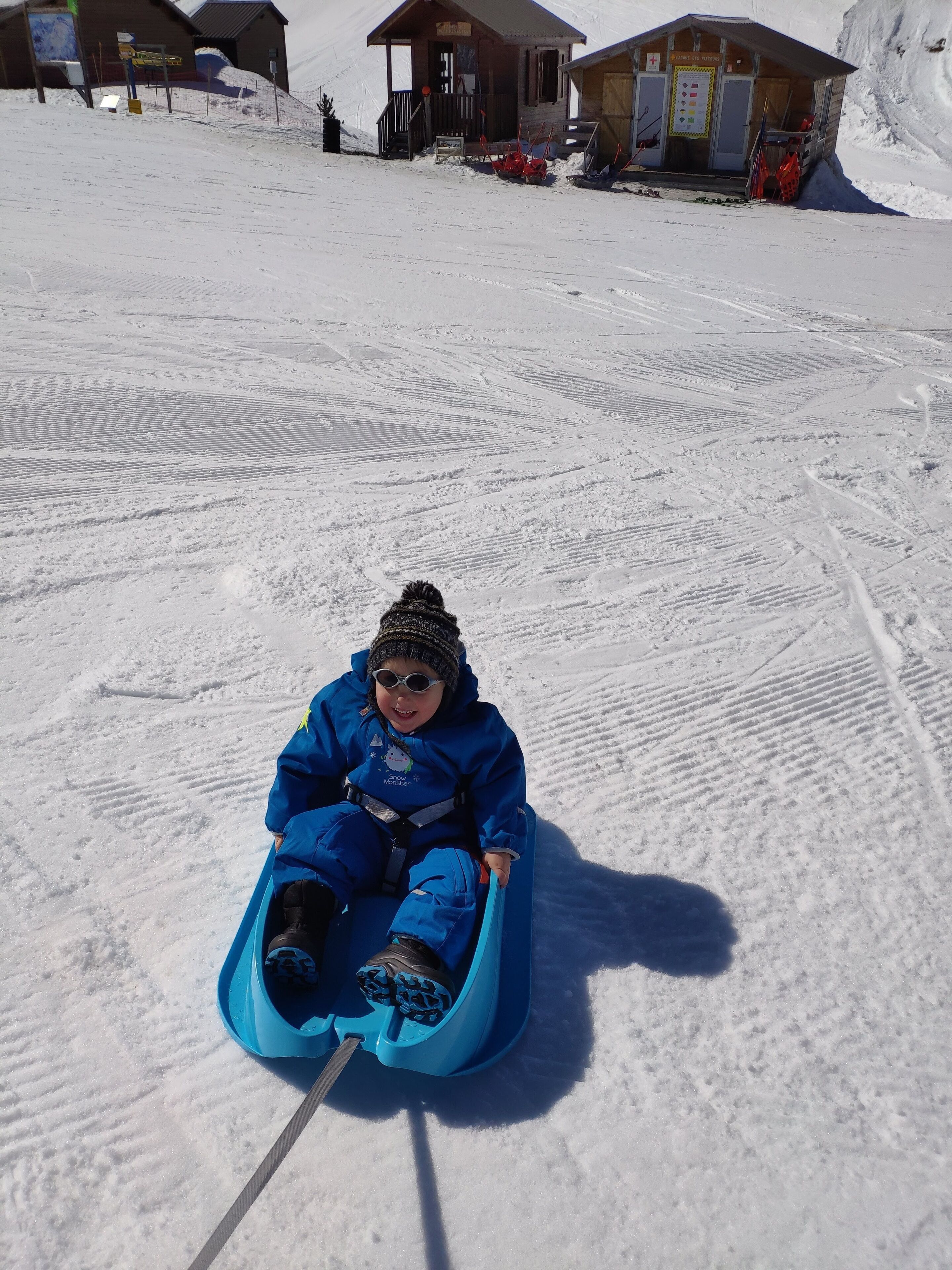 A child in a blue sled on a snowy slope.