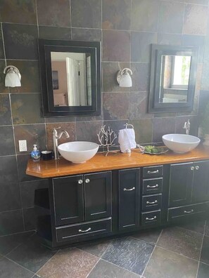 Une salle de bain avec deux lavabos, des murs recouverts de carreaux foncés et un meuble-lavabo en bois doté de placards.