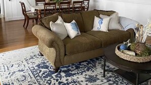 Un soggiorno con un divano marrone, un tappeto decorato, un tavolo da pranzo con sedie e un lampadario.