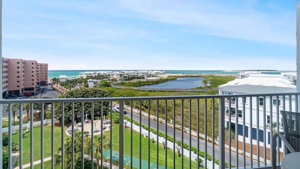 A balcony with a view of a coastal area, including buildings, a road, and a water body.