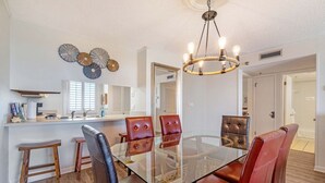 A dining area with a glass table, leather chairs, a chandelier, and decorative wall art.