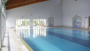 An indoor swimming pool with clear water, wooden beams on the ceiling, and decorative murals on the walls. - Charming, comfortable apartment in a good location (Portimão)
