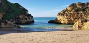 A beach with a sandy shore, rocky cliffs, and calm sea.