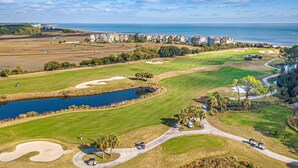 Un parcours de golf avec des bunkers de sable, un étang et une vue sur l’océan.