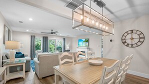 Un espace repas avec une table en bois, des chaises blanches et un lustre moderne.