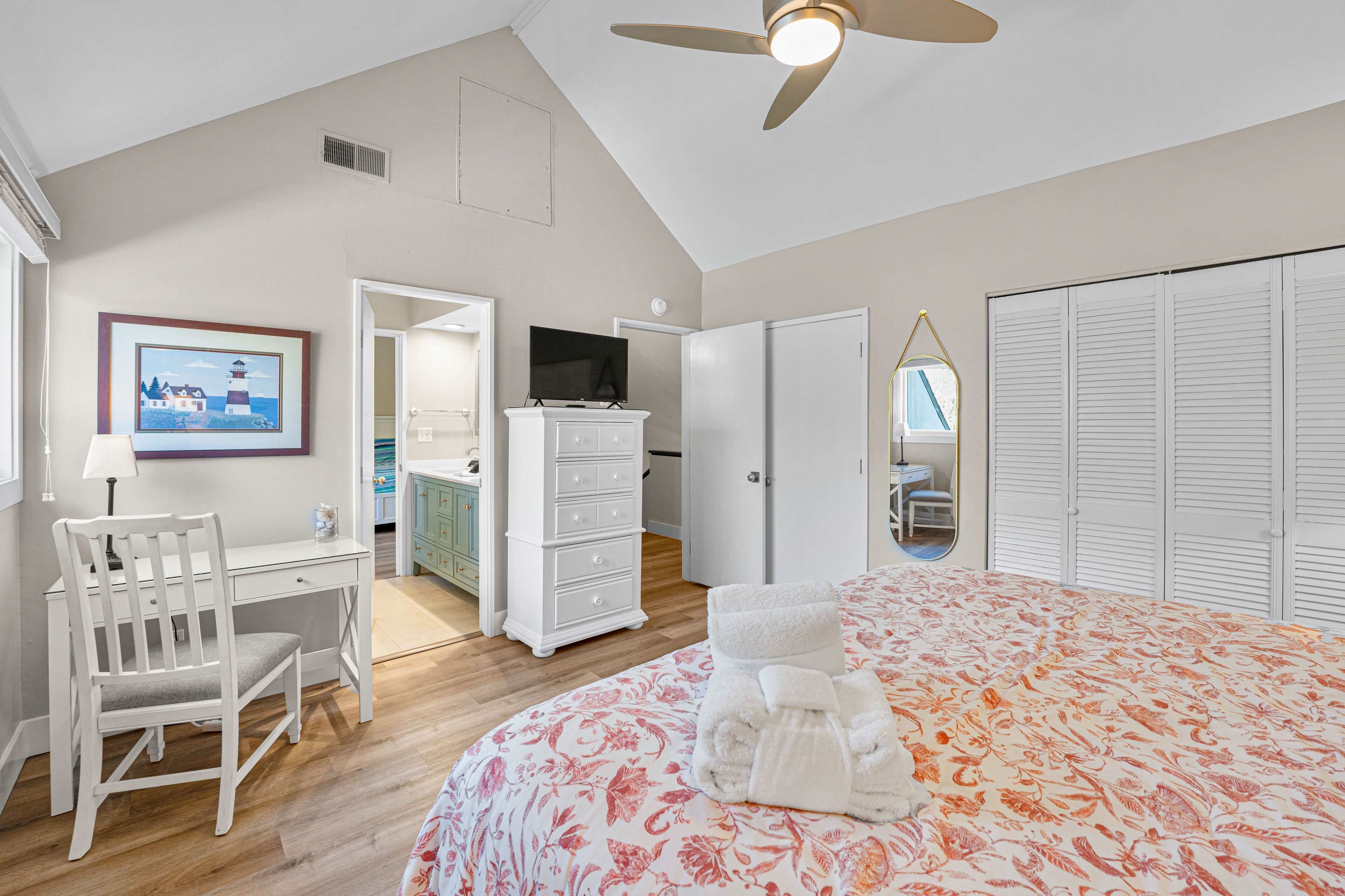 A bedroom with a bed, a desk, a chair, a dresser, a television, and a closet.