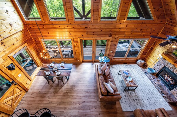 A spacious wooden cabin with a high ceiling, large windows, a cozy seating area, and a fireplace.