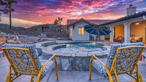 A pool area with two chairs, a patio umbrella, and a house in the background. - 25% off 7-night stay Epic Pool/Spa  Joshua Trees🌵3 King beds 🛌Queen🚶🏿Hiking! (Yucca Valley)