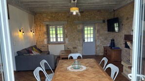 Un coin repas chaleureux avec une table en bois et des chaises blanches, un mur en pierre et un téléviseur fixé au mur.