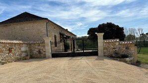 Un bâtiment en pierre avec une allée en gravier et un portail en métal noir.