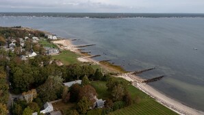 An aerial view of a coastal area with a beach, houses, and a rocky breakwater.
