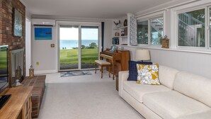 A living room with a piano, a white sofa, a wooden coffee table, and a view of the ocean through a glass door.