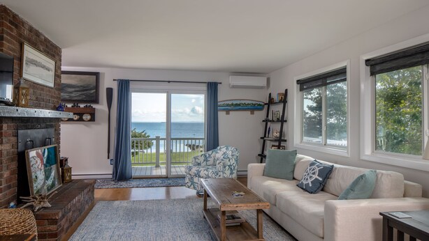 A living room with a fireplace, a sofa, a coffee table, and a view of the sea through large windows.