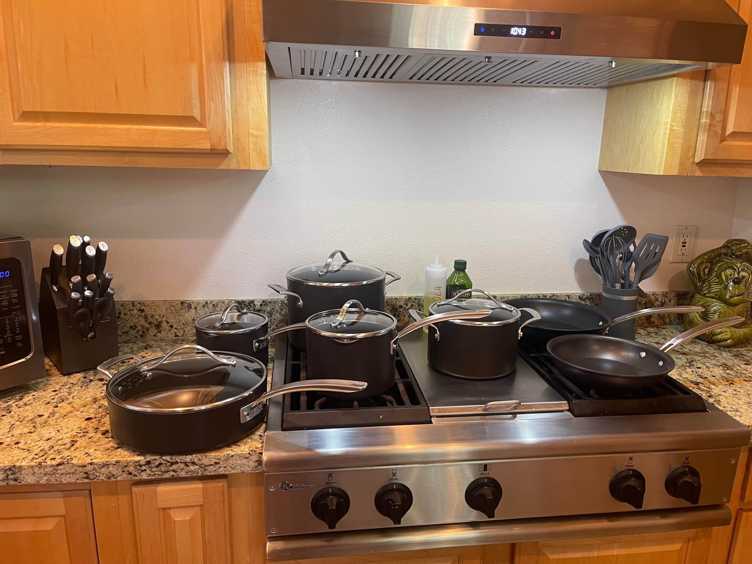 A kitchen with a stainless steel stove, pots, pans, and a knife block.