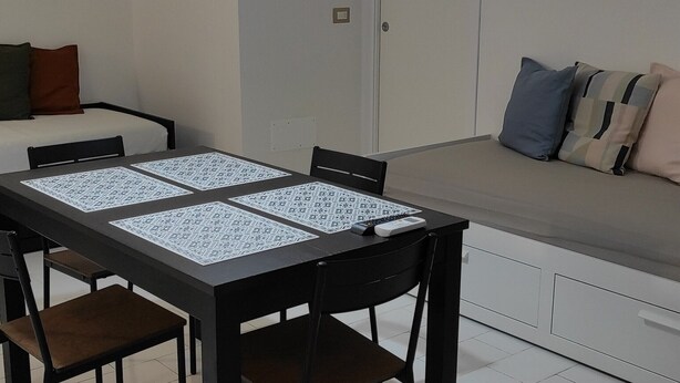 Un coin repas avec une table et des chaises, un luminaire suspendu, un canapé avec des coussins et une porte en arrière-plan.