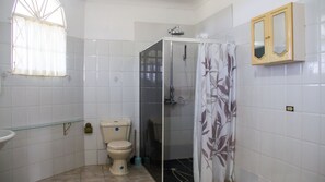 A bathroom with white tiled walls, a toilet, a glass-enclosed shower, and a wooden cabinet with a mirror.