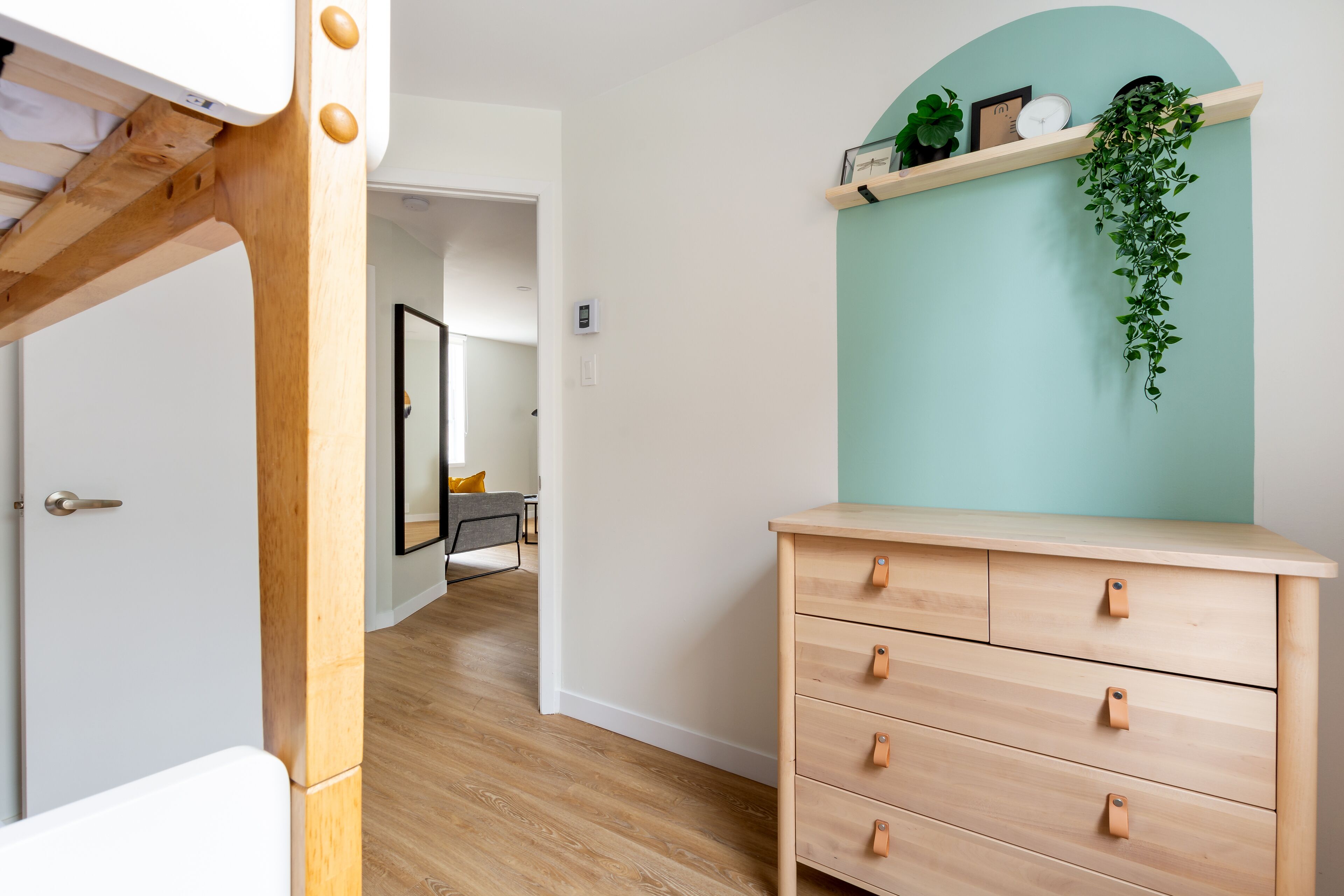 Una habitación con cómoda de madera, pared decorada en color aguamarina y planta colgante.