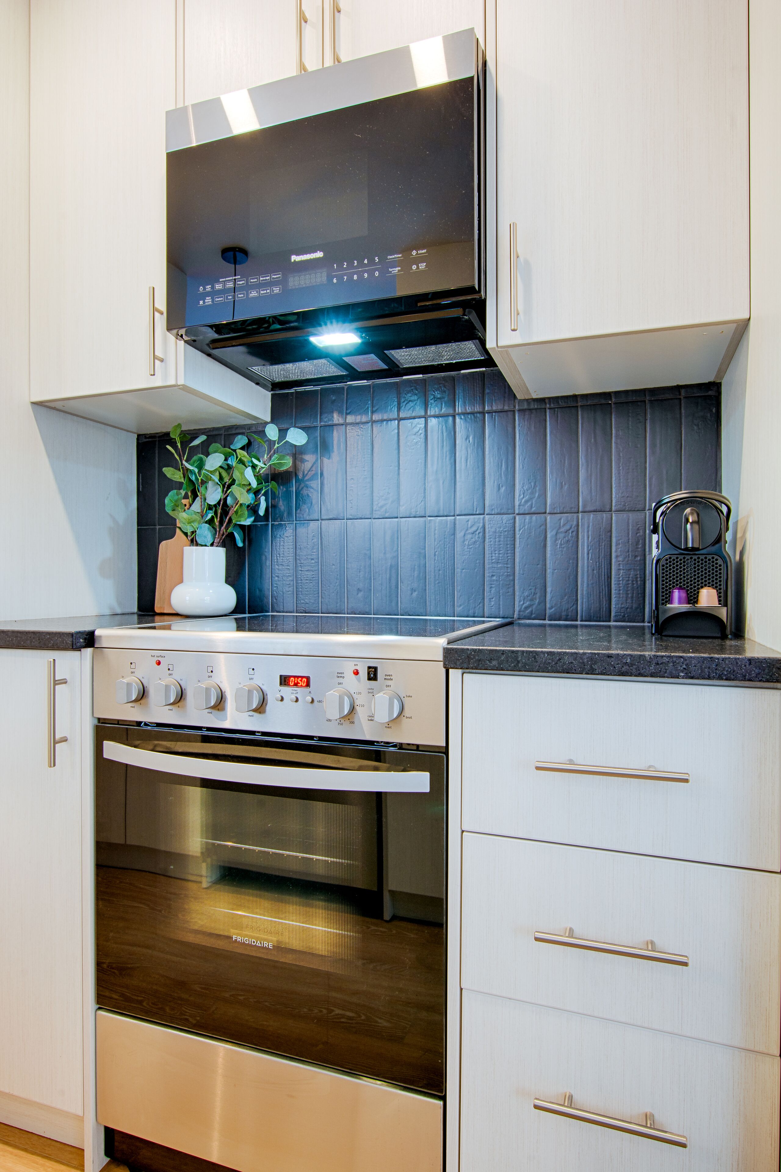 Una cocina con estufa, horno y microondas de acero inoxidable. Hay una planta en maceta sobre la encimera y una cafetera.