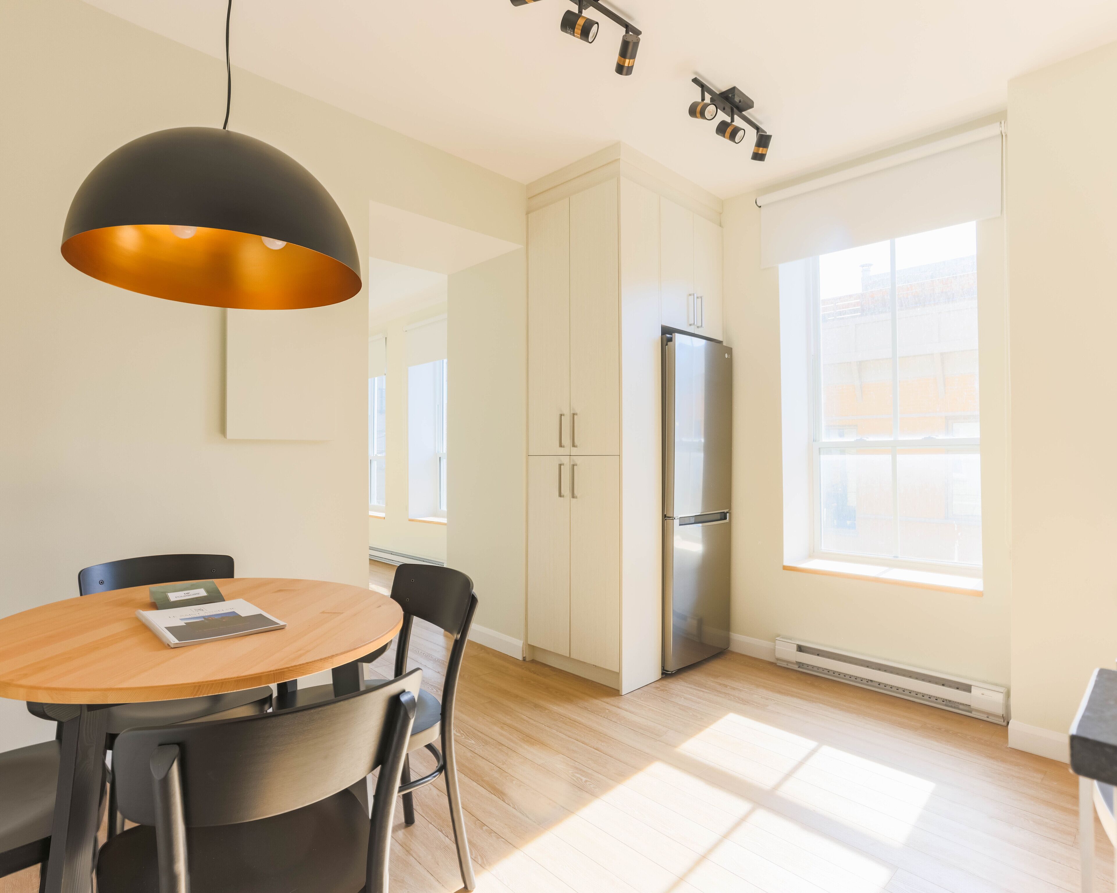 Eine moderne Küche mit Esstisch, Stühlen, einem Kühlschrank und Pendelleuchten.