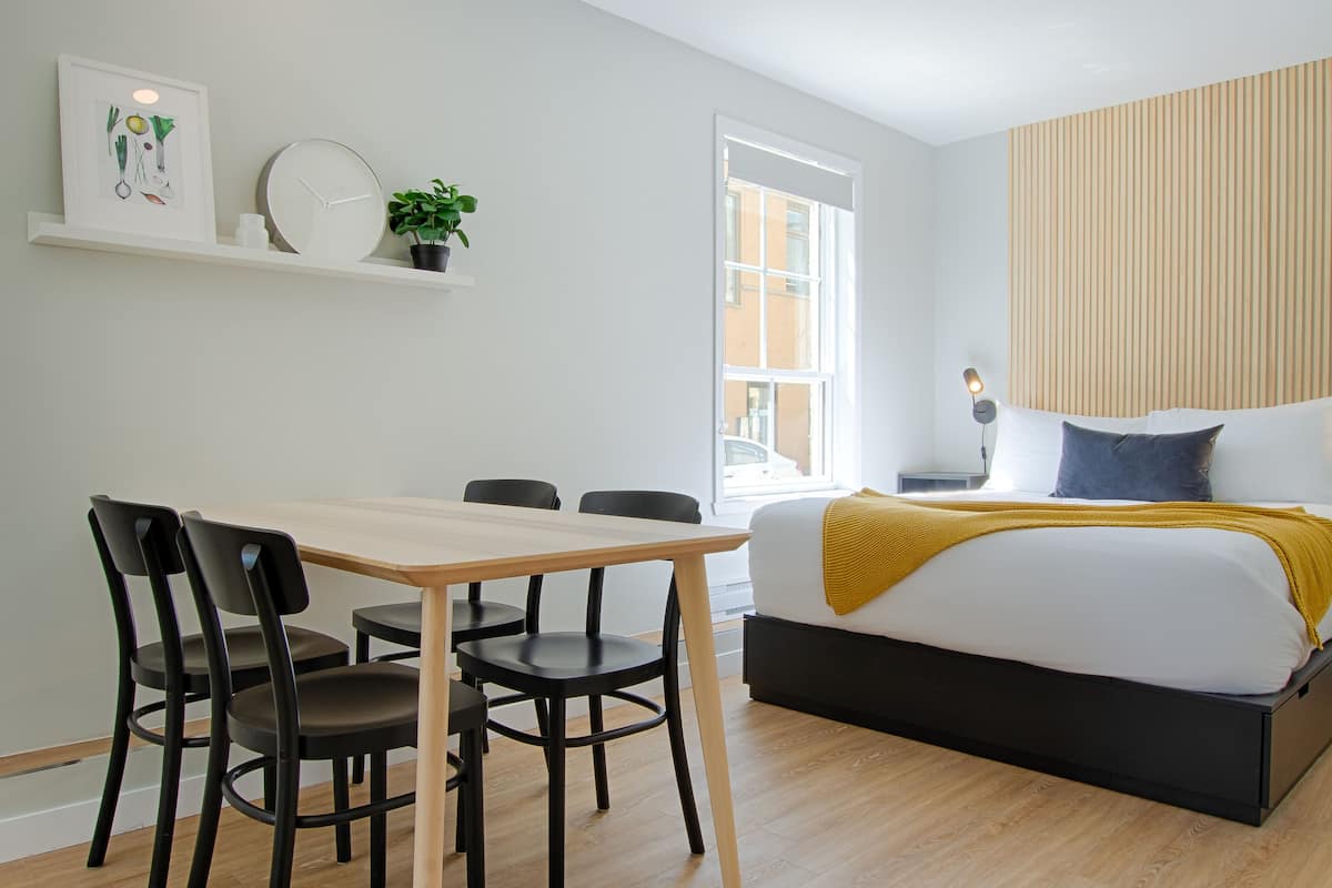 Une chambre moderne avec un lit, une table de chevet, une lampe et une fenêtre donnant sur la rue.
