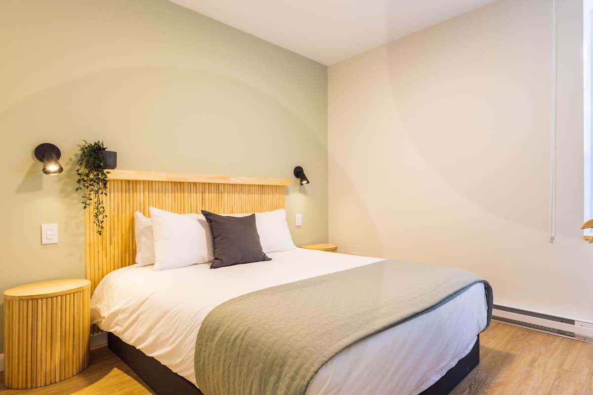Une chambre à coucher bien rangée, avec un lit, des tables de chevet, une lampe fixée au mur et une plante en pot.