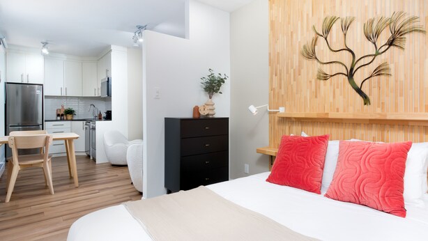 A modern hotel room with a bed, a desk, and a kitchenette.