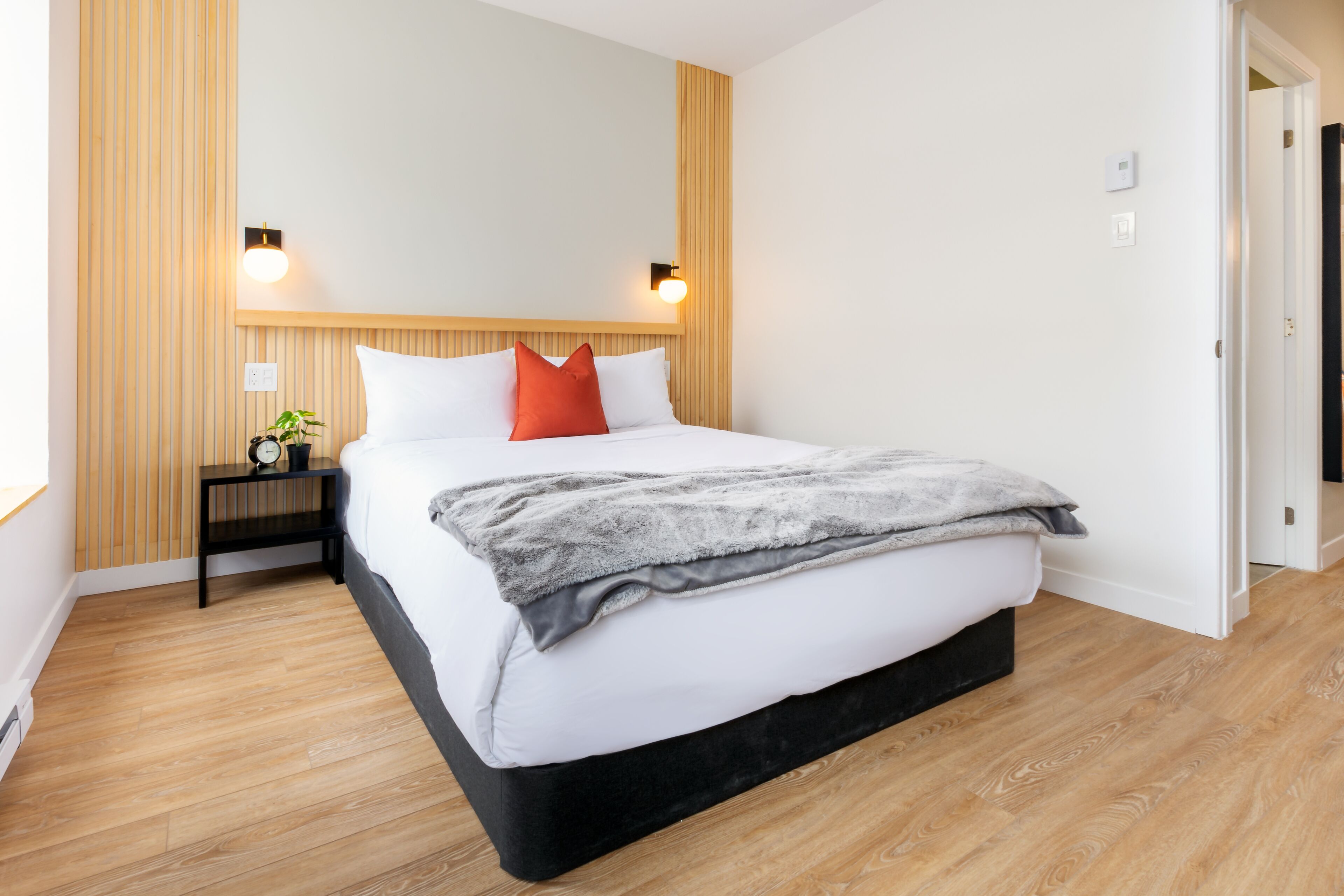 A modern bedroom with a large bed, wooden panel walls, and two bedside lamps.