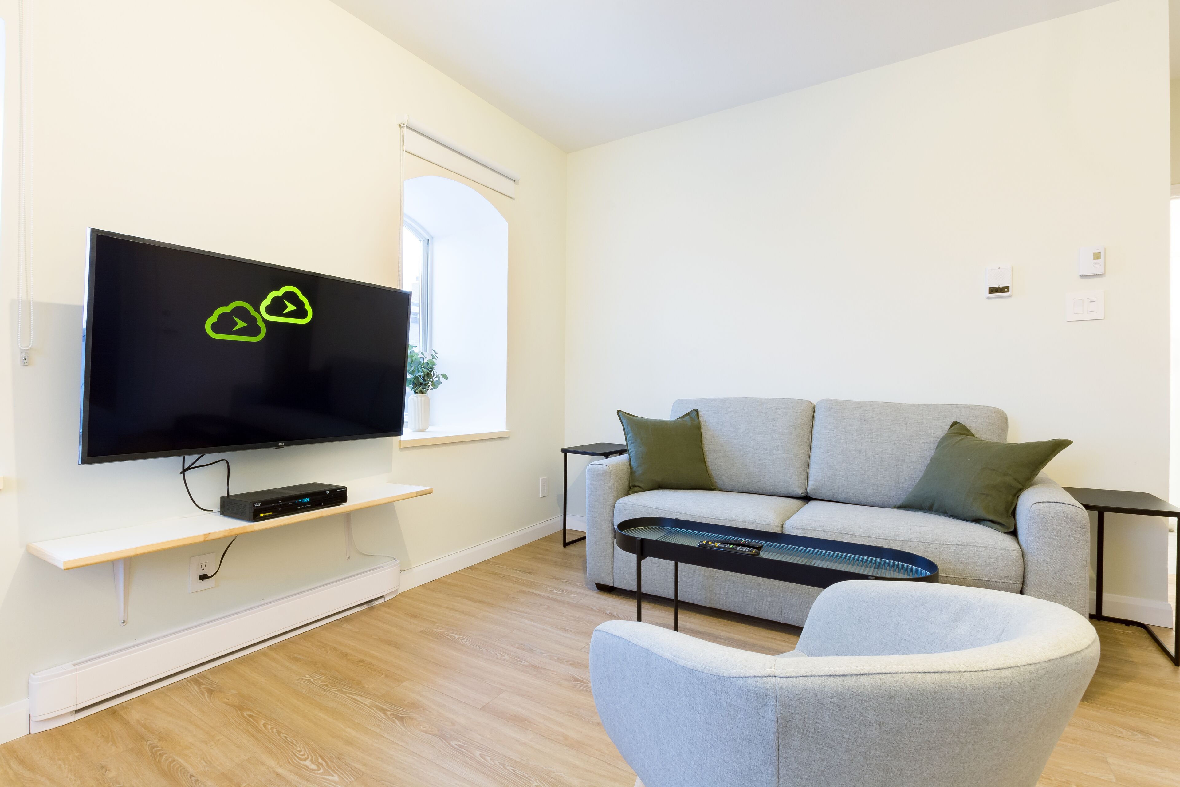 A modern living room with a flat-screen TV, a grey sofa, a small coffee table, and a grey armchair.
