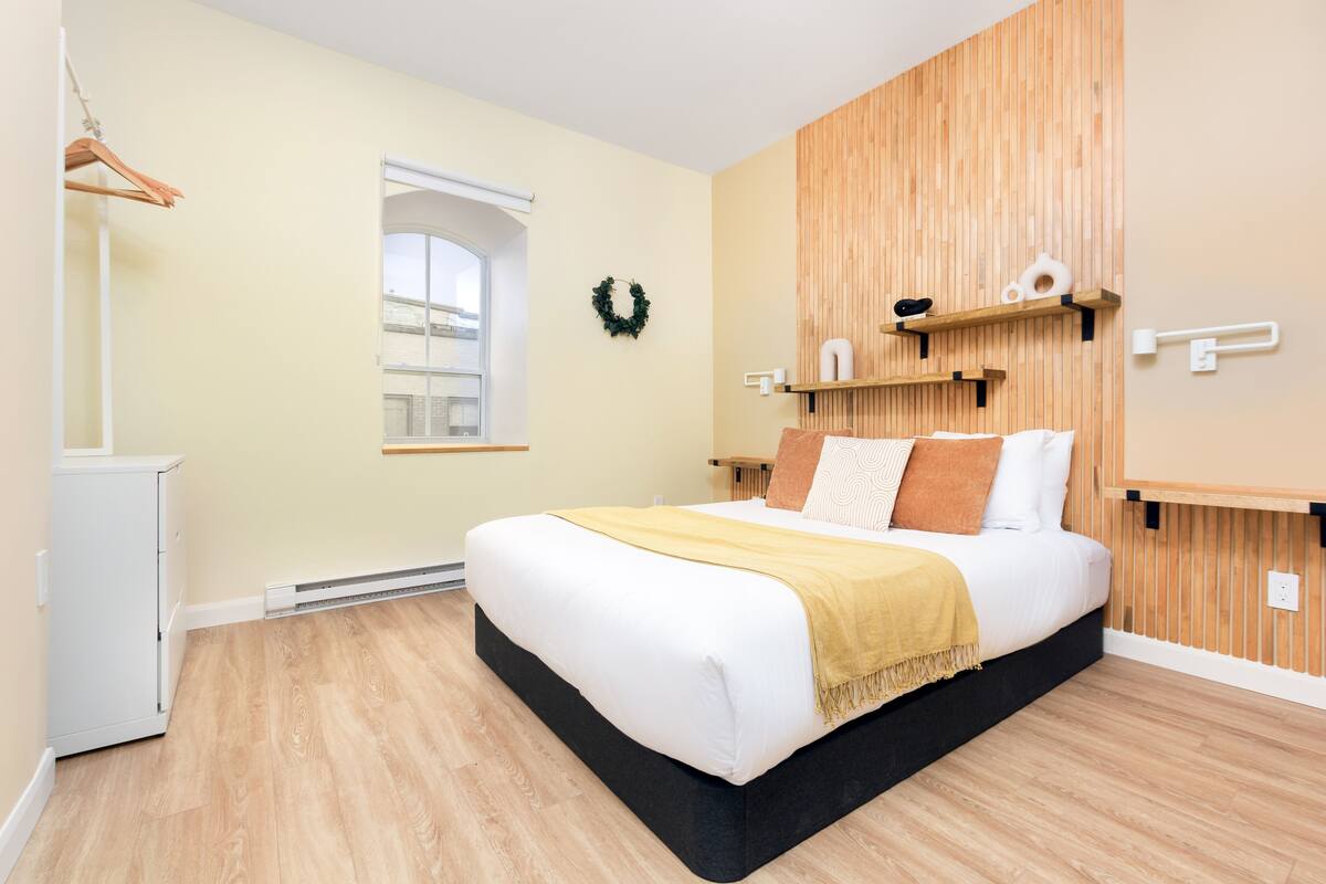Une chambre moderne avec un grand lit, un mur recouvert de panneaux en bois et une petite fenêtre.
