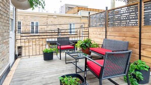 A covered patio with outdoor furniture, potted plants, and a view of the cityscape.