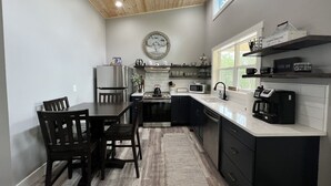 A modern kitchen with a wooden ceiling, a dining area with a table and chairs, and a coffee station.