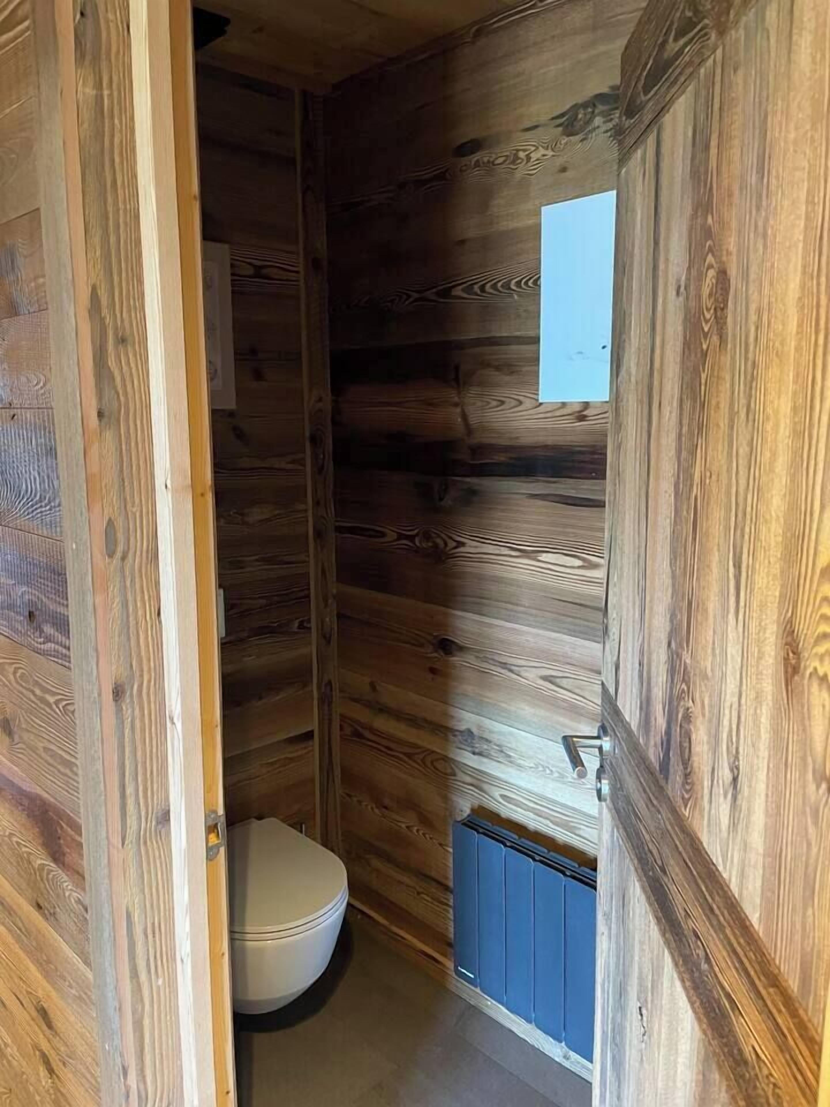 A wooden cabin-style bathroom with a toilet and a small window.