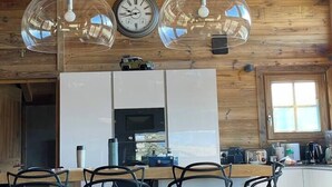 Interior de madeira com cozinha, incluindo uma mesa de jantar com cadeiras, um relógio e luminárias pendentes.