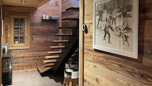 Interior em madeira com escada, um quadro na parede e uma janela com persianas.