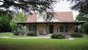 A stone house with a covered porch, a small front yard, and a well-maintained lawn. - Dos Pinos Riverside Cottage near DT Kerrville (Kerrville)
