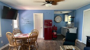 Un comedor con una mesa y sillas de madera, un refrigerador rojo, un reloj en la pared y un ventilador de techo.