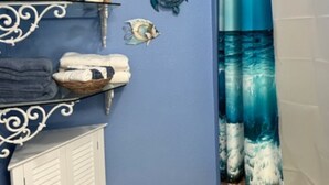 Un baño con pared azul, tocador blanco y cortina de ducha con diseño de olas.