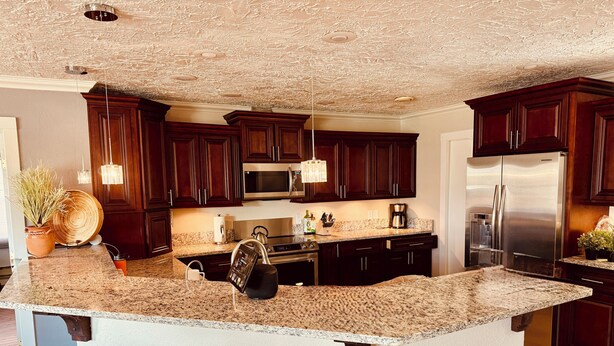 A kitchen with dark wood cabinets, stainless steel appliances, granite countertops, and pendant lighting.