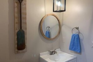 A bathroom with a white sink, a round mirror, and a blue towel hanging on a ring. - Cottage Too at JP Coleman - 5 min from JP Coleman State Park (Iuka)