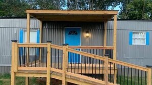 Una terraza de madera con una rampa que lleva a una puerta azul, rodeada de vallas metálicas.
