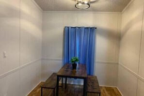 A small room with a wooden table and chairs, a potted plant, and a blue curtain. - Cottage Too at JP Coleman - 5 min from JP Coleman State Park (Iuka)