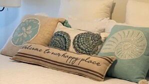 A bed with a quilted white duvet, a pillow with a 'Welcome to our happy place' text, and decorative pillows with shell designs. - Cozy and relaxing beach house, Our Little Pearl in Foley. (Foley)