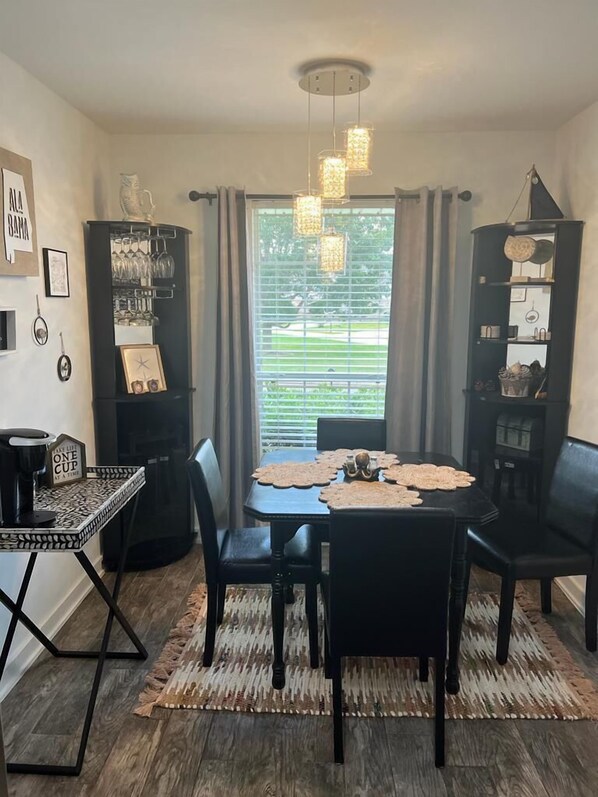A dining area with a table set for four, surrounded by chairs, with a black cabinet to the left and a black shelving unit to the right. - Cozy and relaxing beach house, Our Little Pearl in Foley. (Foley)